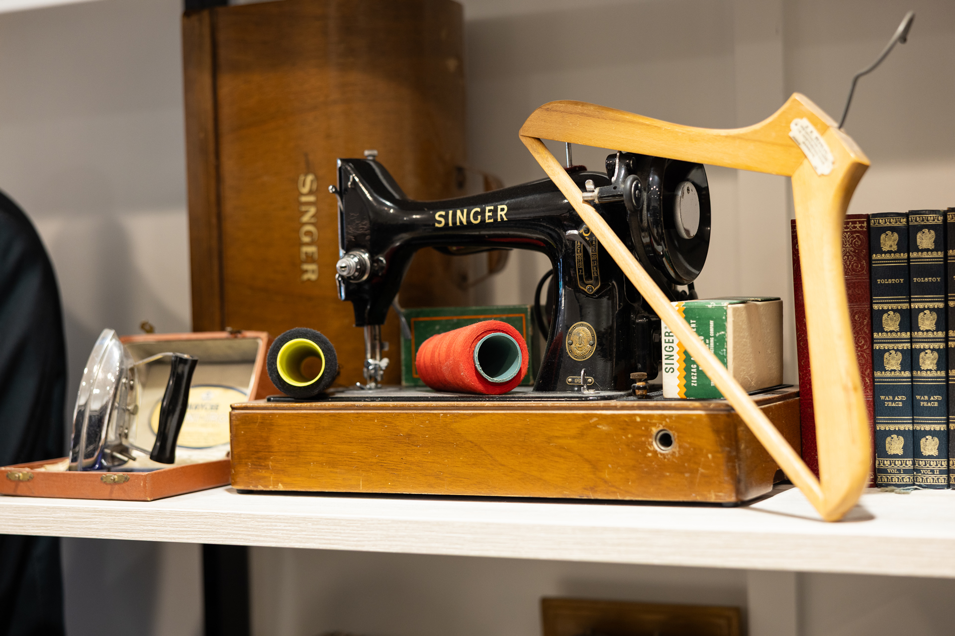 A vintage Singer sewing machine on a shelf with thread, a wooden hanger and a flat iron