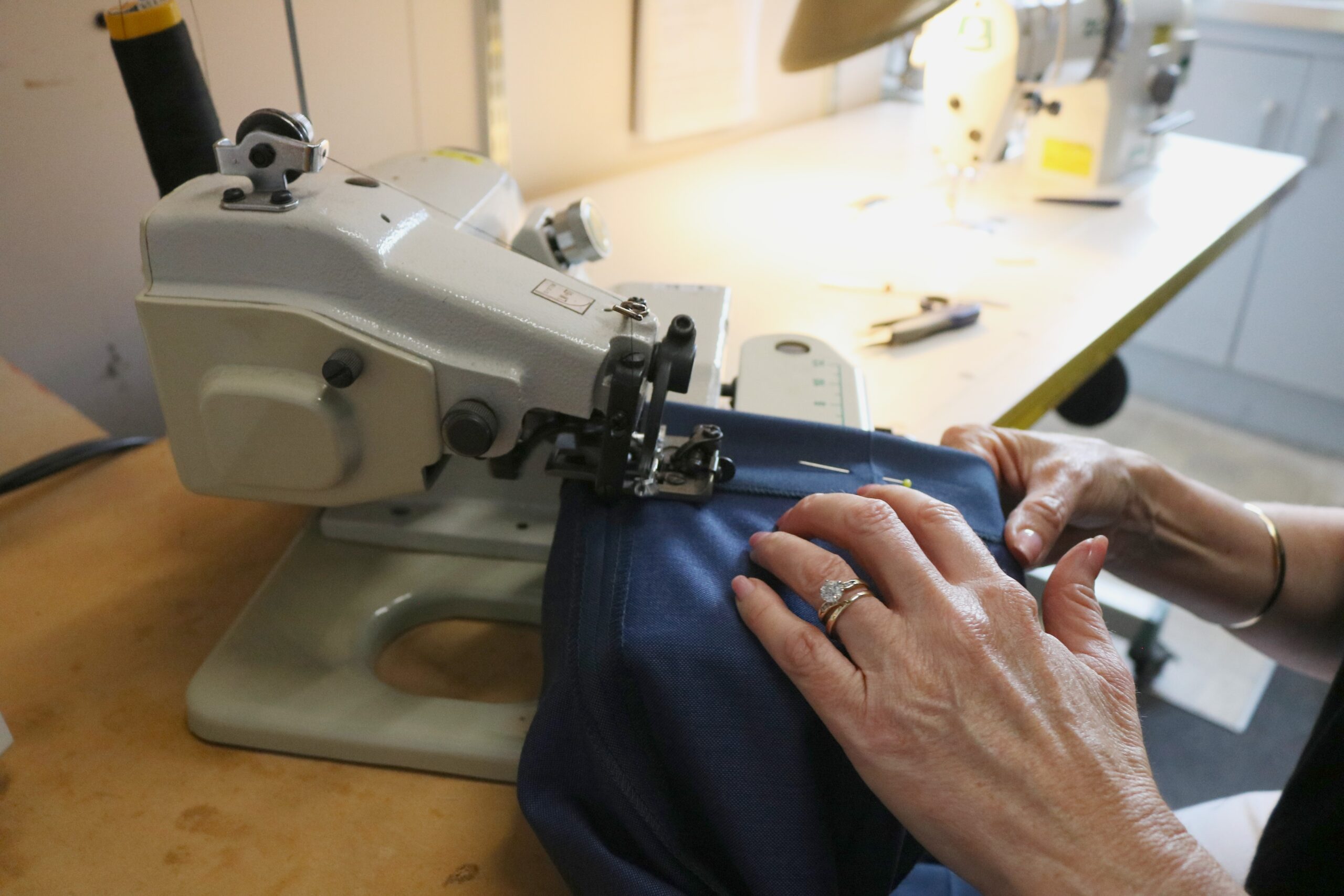 Hands guiding navy cloth through a blind hemming machine in the Bond & Co workroom