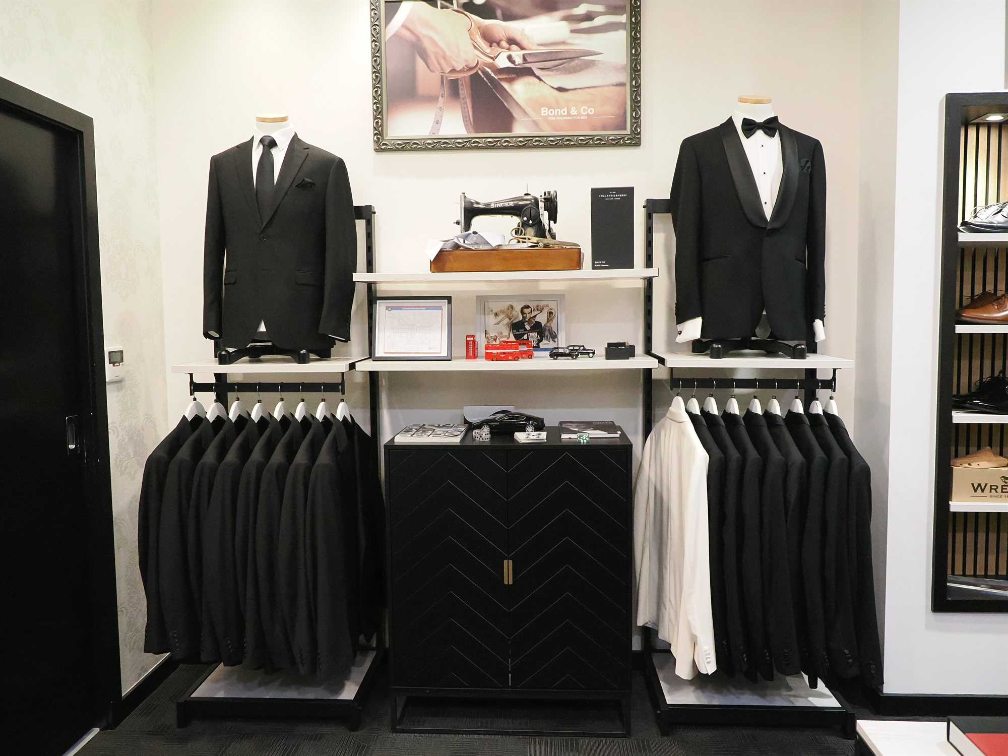 Hire suit rails in store, a black suit and a shawl collar dinner suit displayed on mannequins above racks of black and white jackets